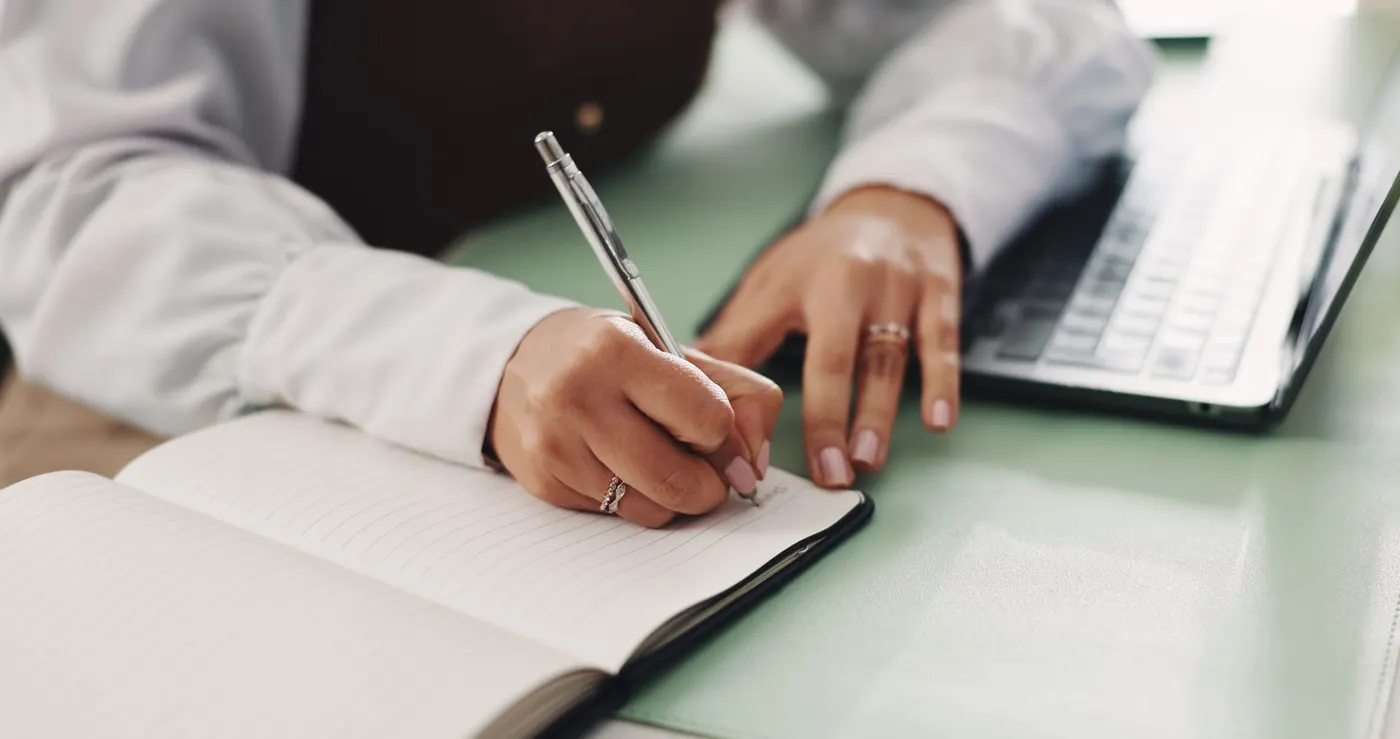 Mains écrivant une note personnalisée à côté d'un ordinateur.