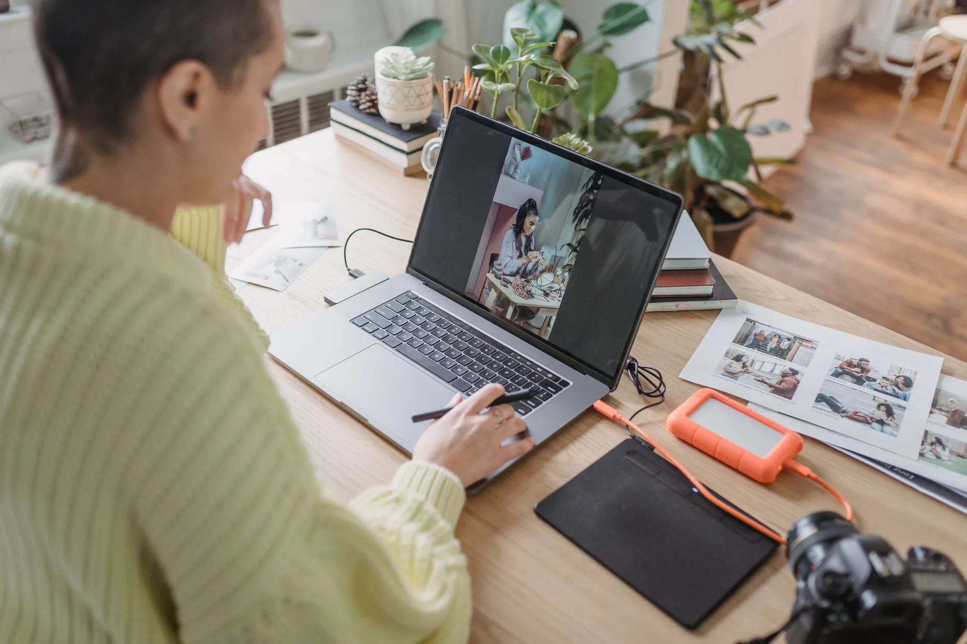 Graphiste retouchant une photo sur son ordinateur avec une tablette graphique et des tirages posés sur le bureau