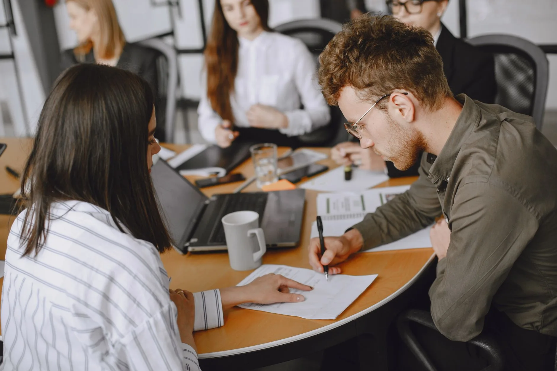 Équipe réunie autour d'une table de travail annote des dossiers papier à côté d'un ordinateur portable