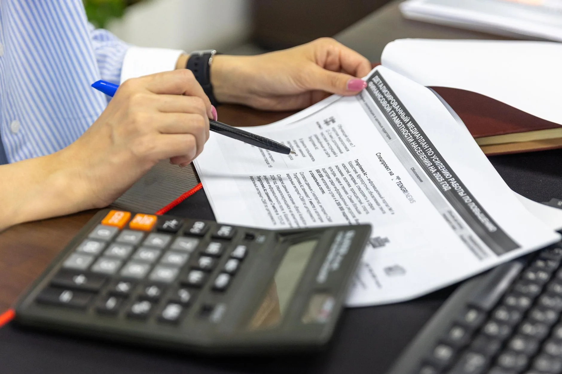 Main annote un relevé financier à côté d'une calculatrice posée sur le bureau