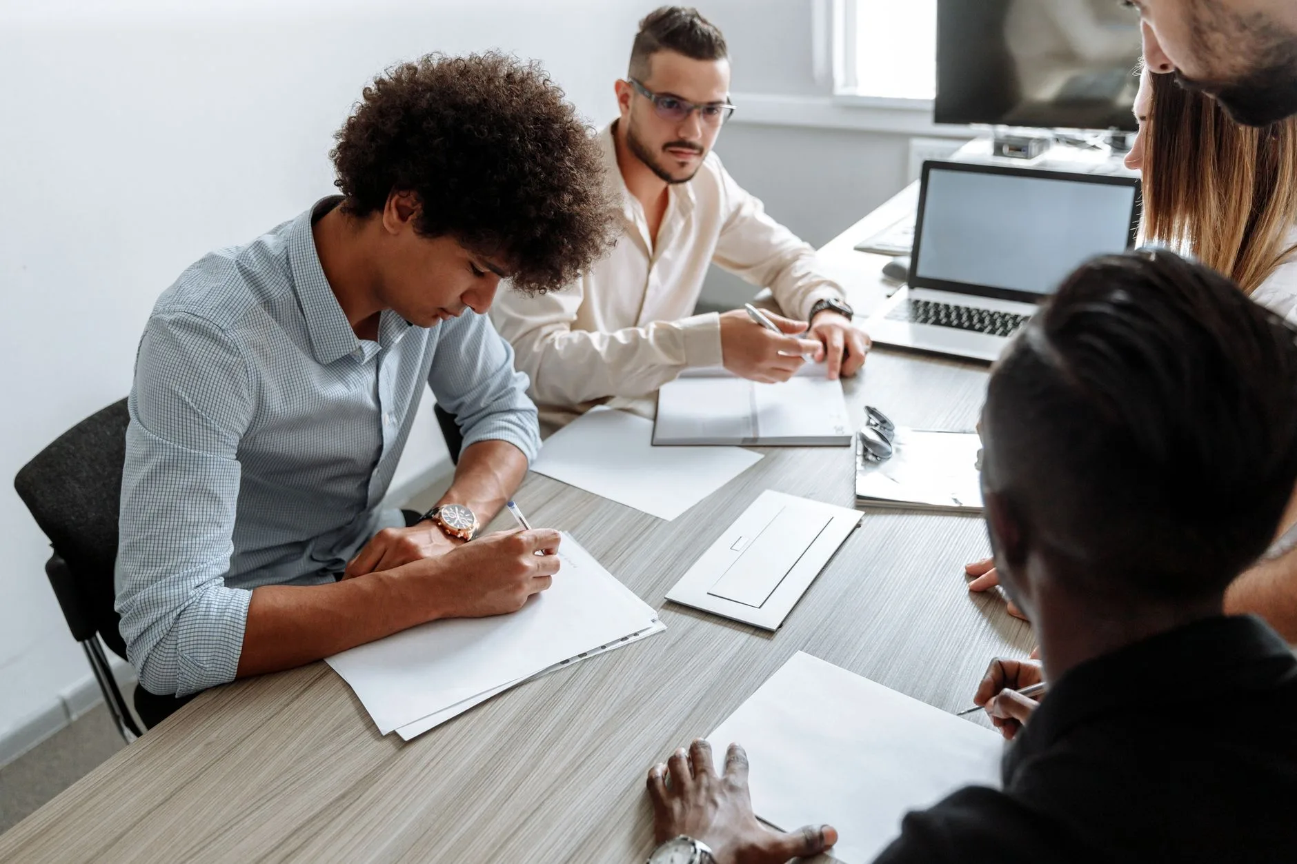 Équipe réunie autour d'une table de travail, prise de notes et ordinateurs portables pour arbitrer un choix d'outil