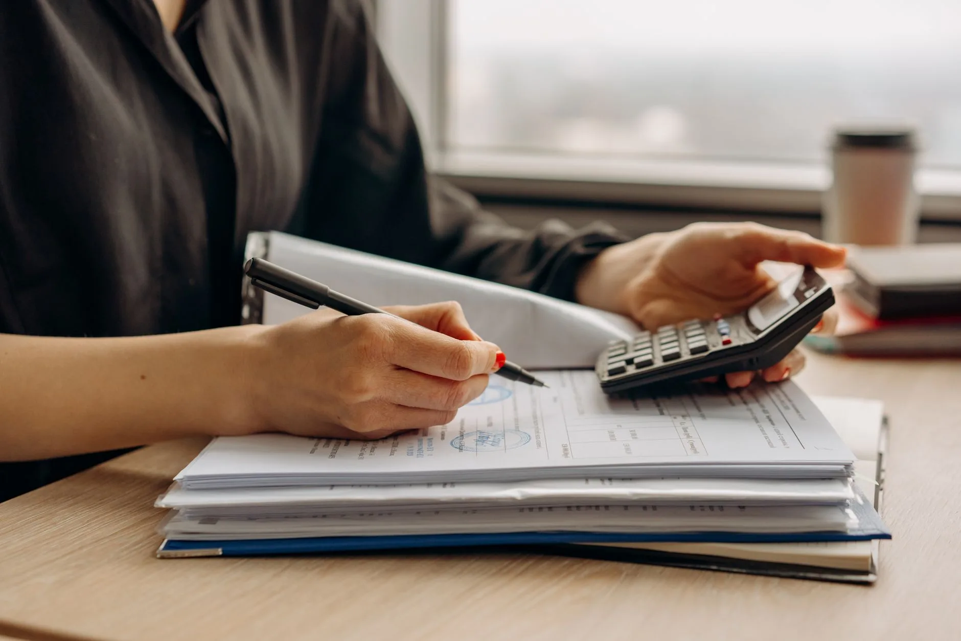 Auditrice pointant une ligne d'un dossier comptable, calculatrice posée sur le bureau