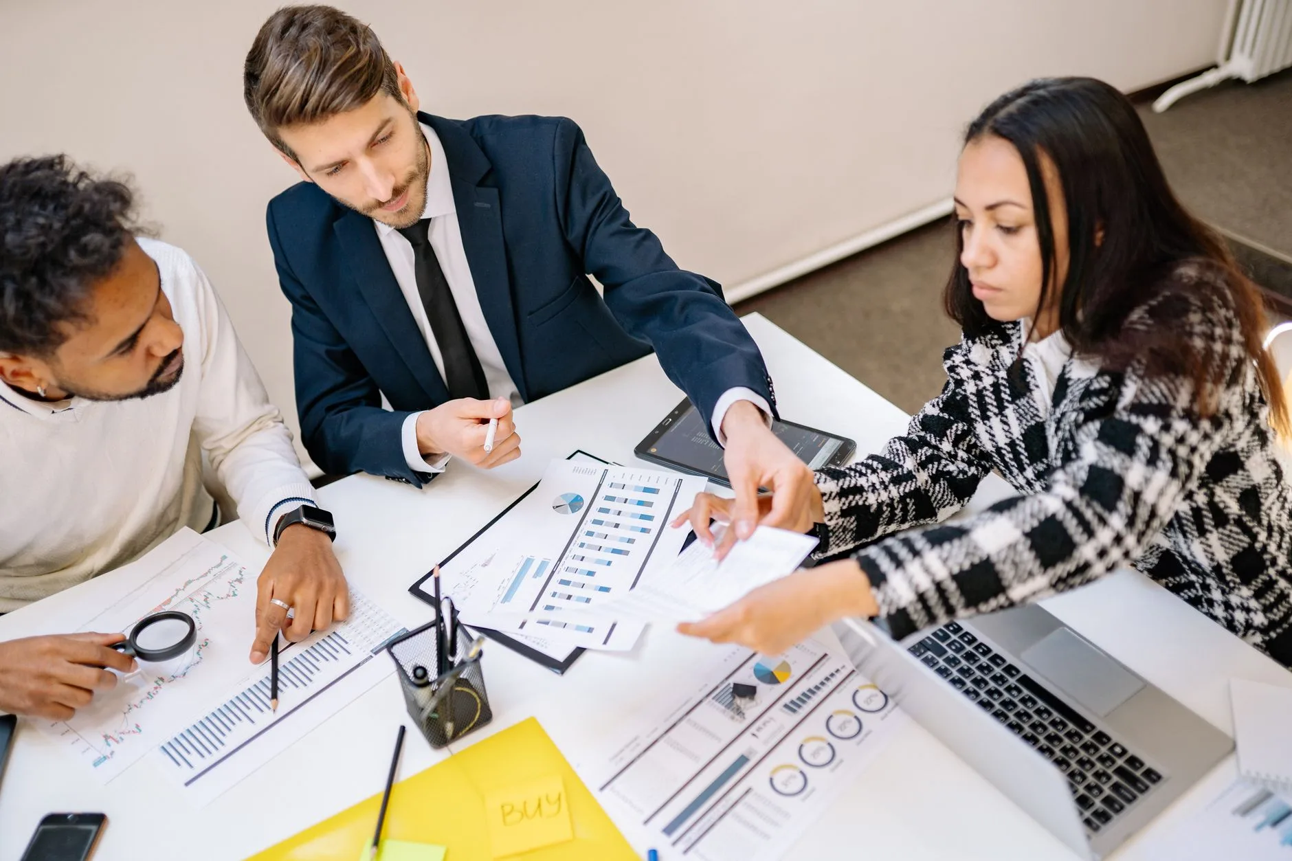 Trois collaborateurs annotent des tableaux de bord imprimés lors d'une réunion de travail