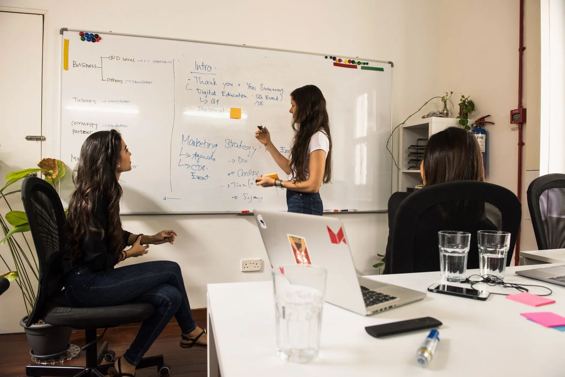 Trois collaboratrices cadrent un projet devant un tableau blanc couvert de notes manuscrites