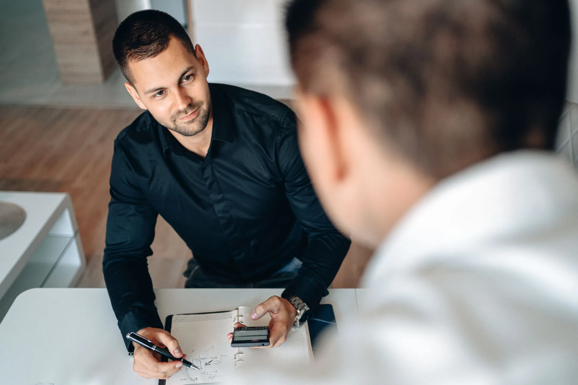 Commercial en chemise noire prend des notes face à un client lors d'un rendez-vous de vente