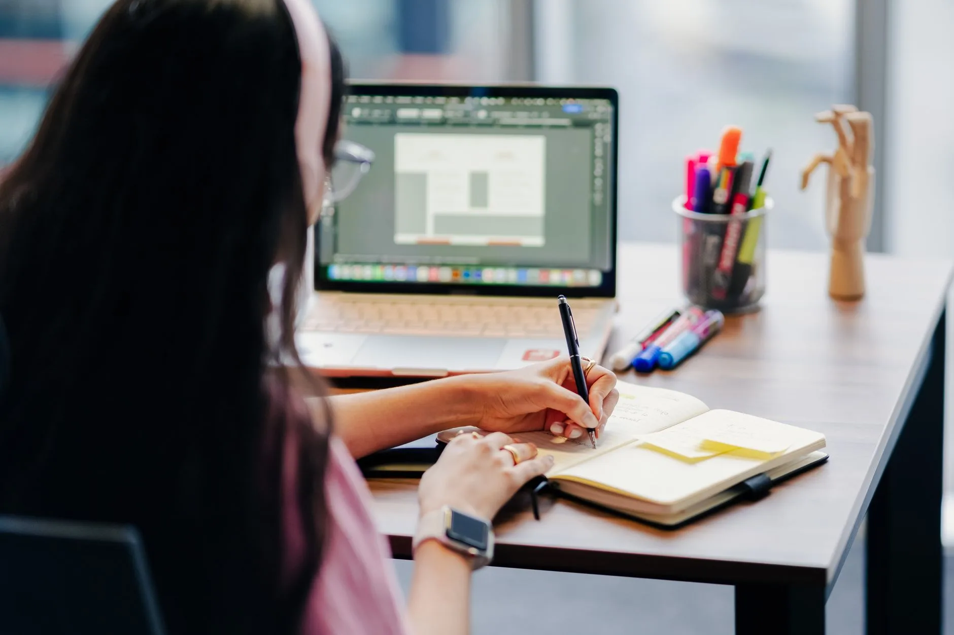 Responsable marketing rédigeant ses critères de qualification sur un carnet devant son ordinateur portable