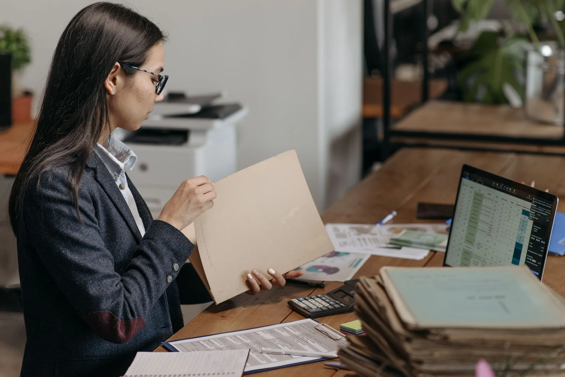 Auditrice consulte un dossier papier devant son ordinateur et des piles de documents comptables