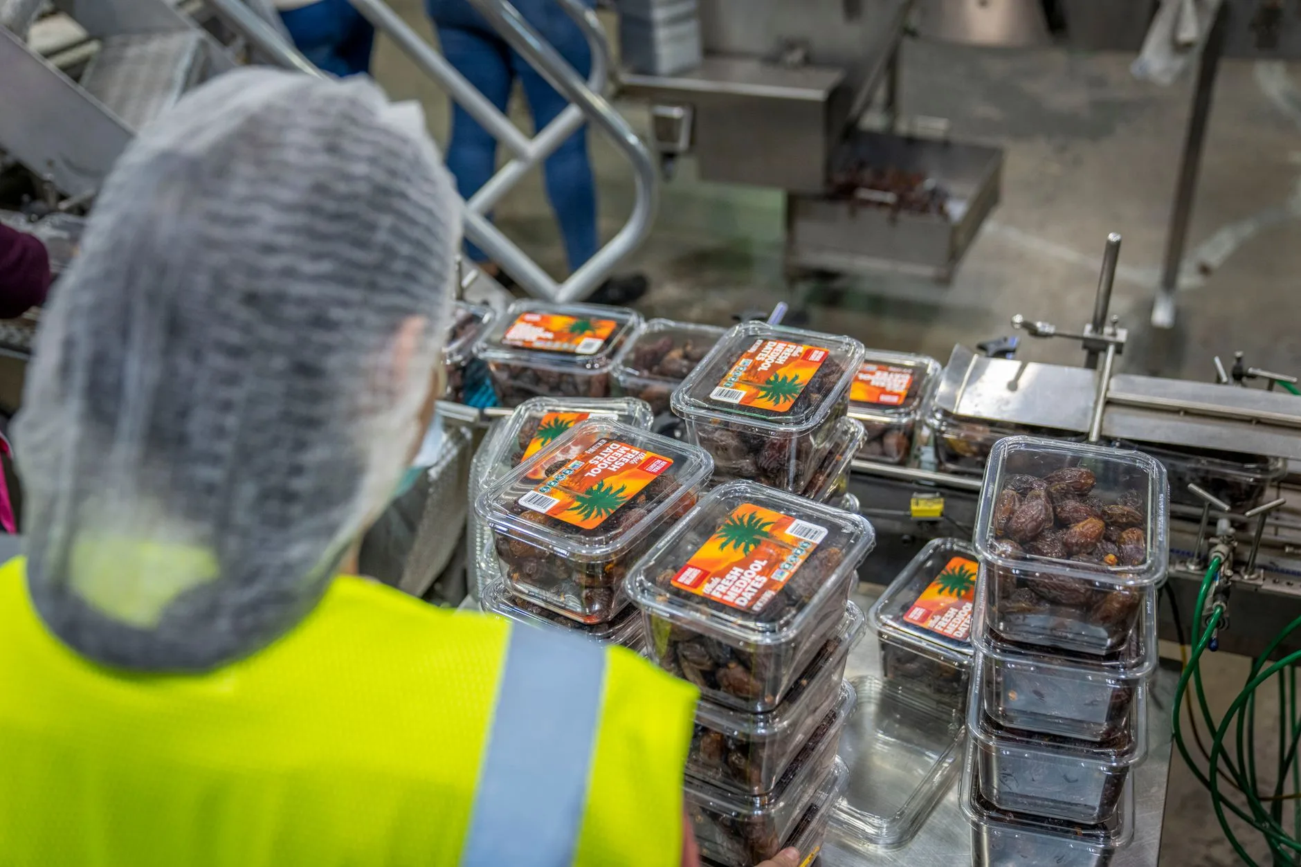 Opératrice en gilet fluo contrôle des barquettes alimentaires sur une ligne de conditionnement
