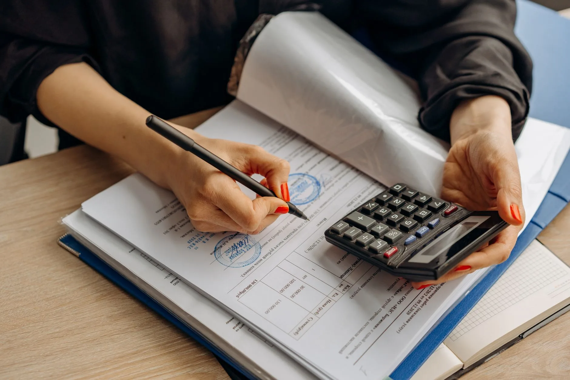 Comptable annote un dossier de chiffrage à la main, calculatrice posée sur le classeur