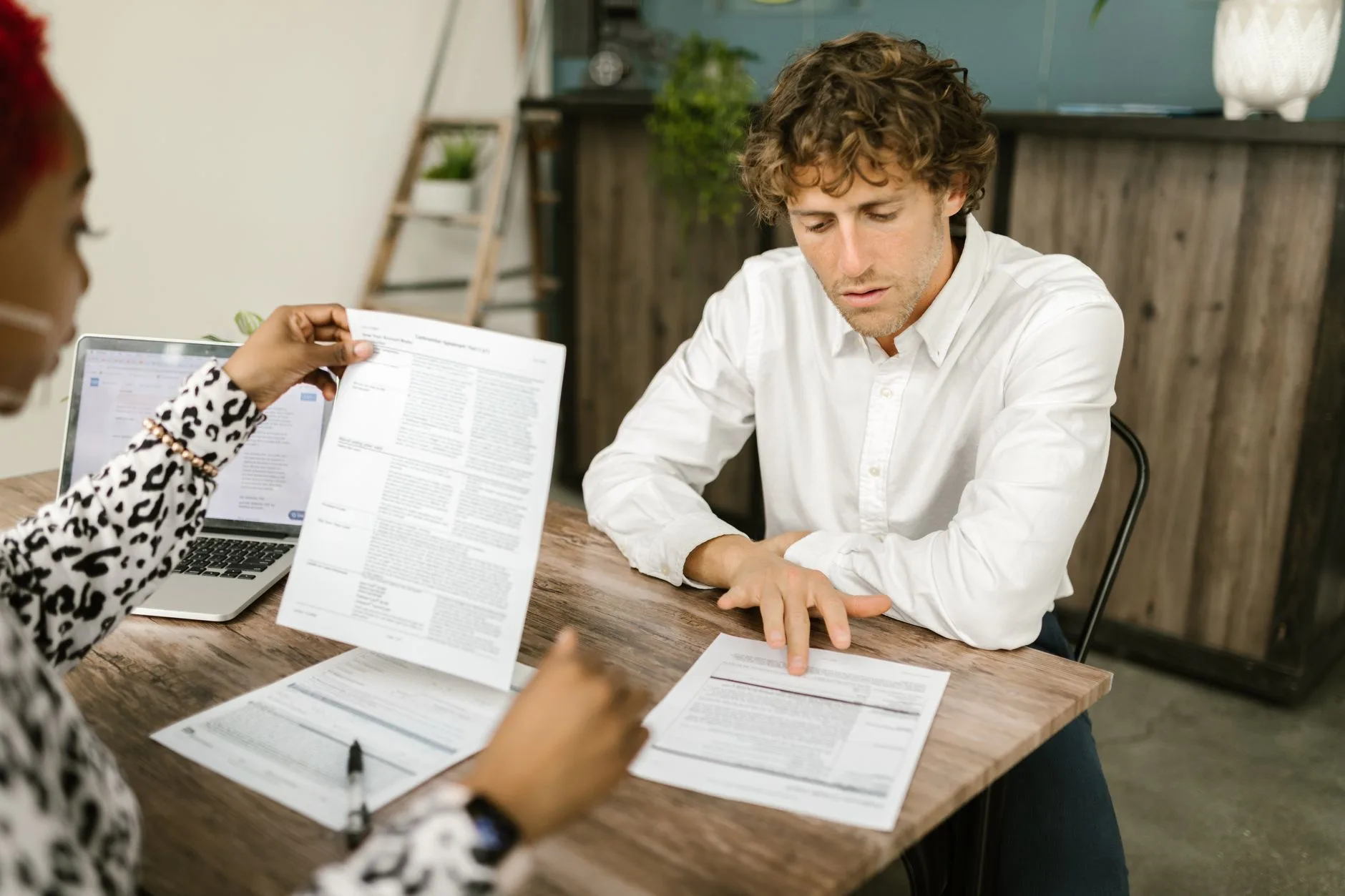 Deux collaborateurs comparent des documents imprimés devant un ordinateur portable au bureau