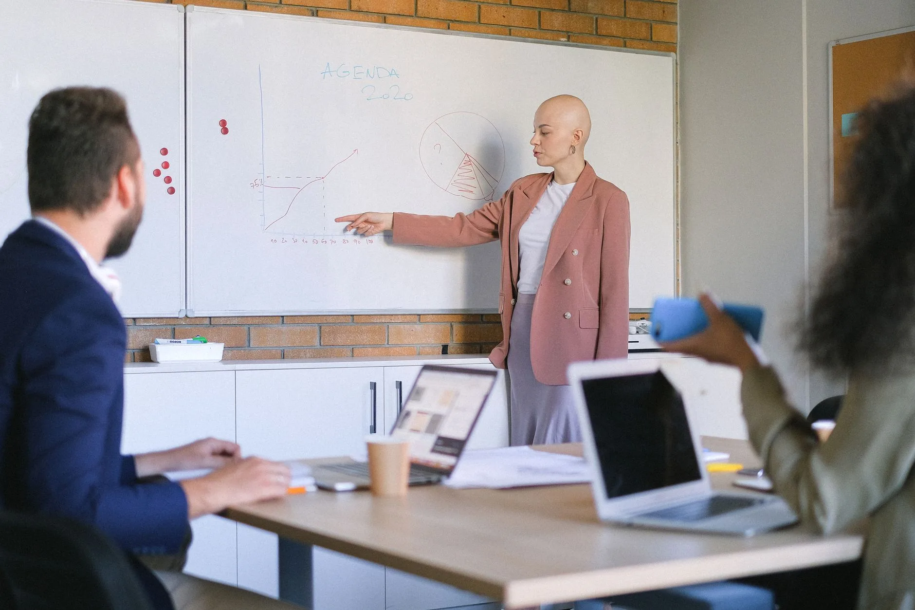 Consultante commentant un schéma tracé au tableau blanc devant trois collègues assis avec leurs ordinateurs