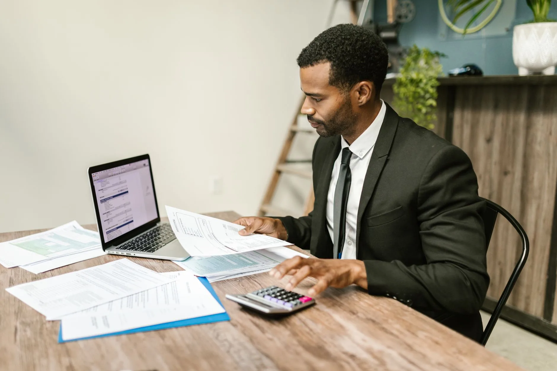 Cadre annote des documents comptables à son bureau, ordinateur portable et calculatrice à portée de main