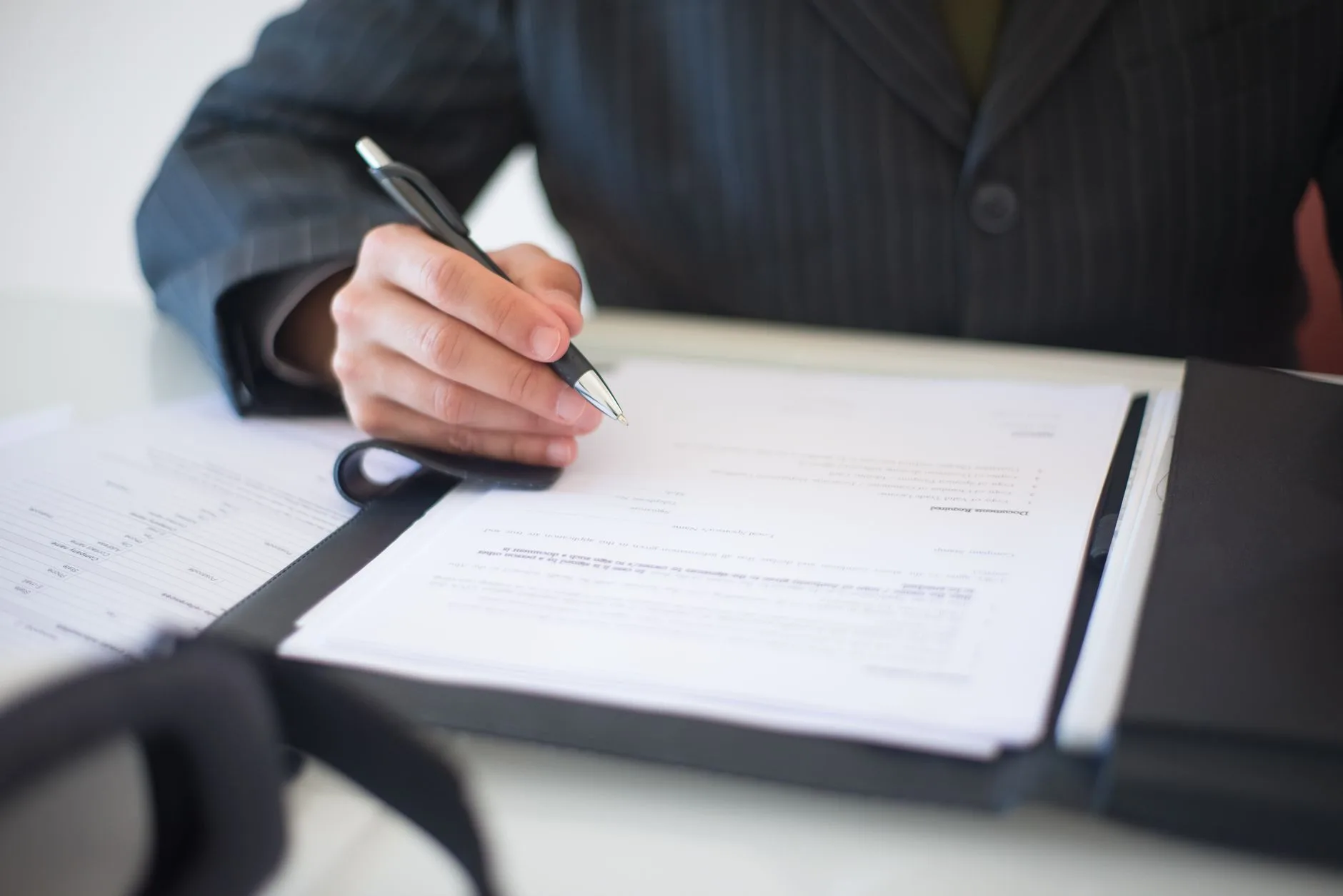 Main tenant un stylo au-dessus d’un contrat de prestation posé sur un bureau