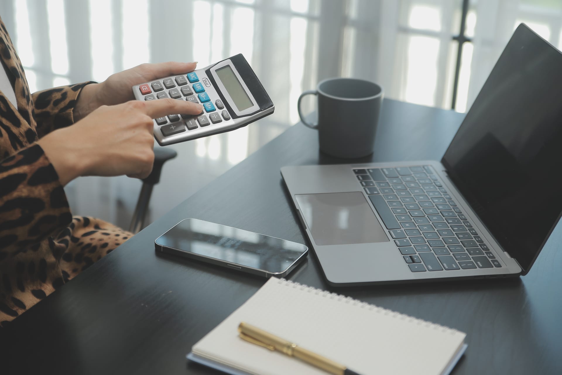 Main utilisant une calculatrice à côté d'un ordinateur portable sur un bureau