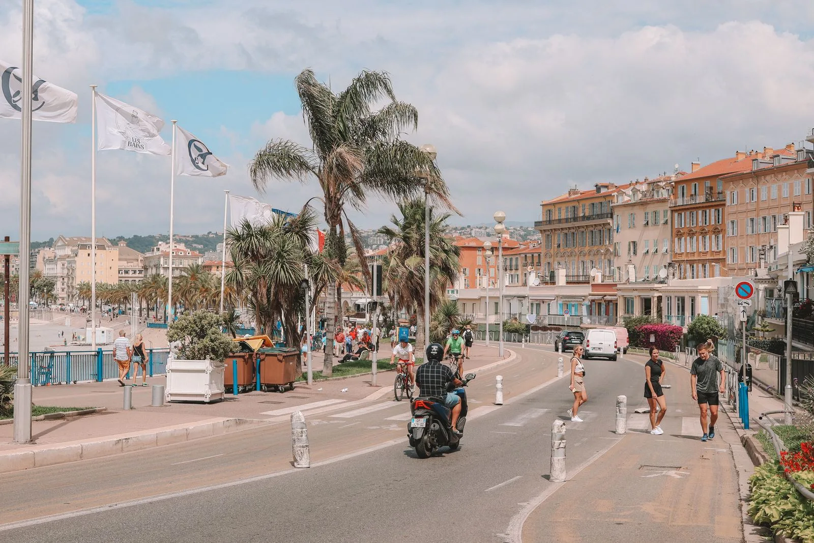 Piétons et scooter sur la promenade des Anglais à Nice, palmiers et façades en bord de mer