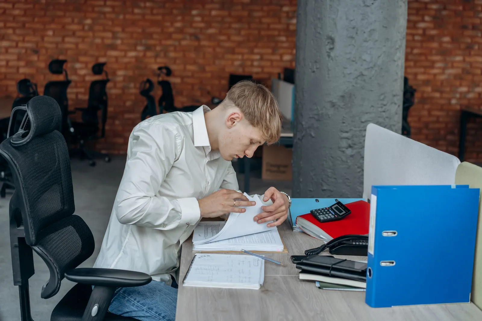 Comptable penché sur une pile de factures à son bureau, classeurs et calculatrice à côté