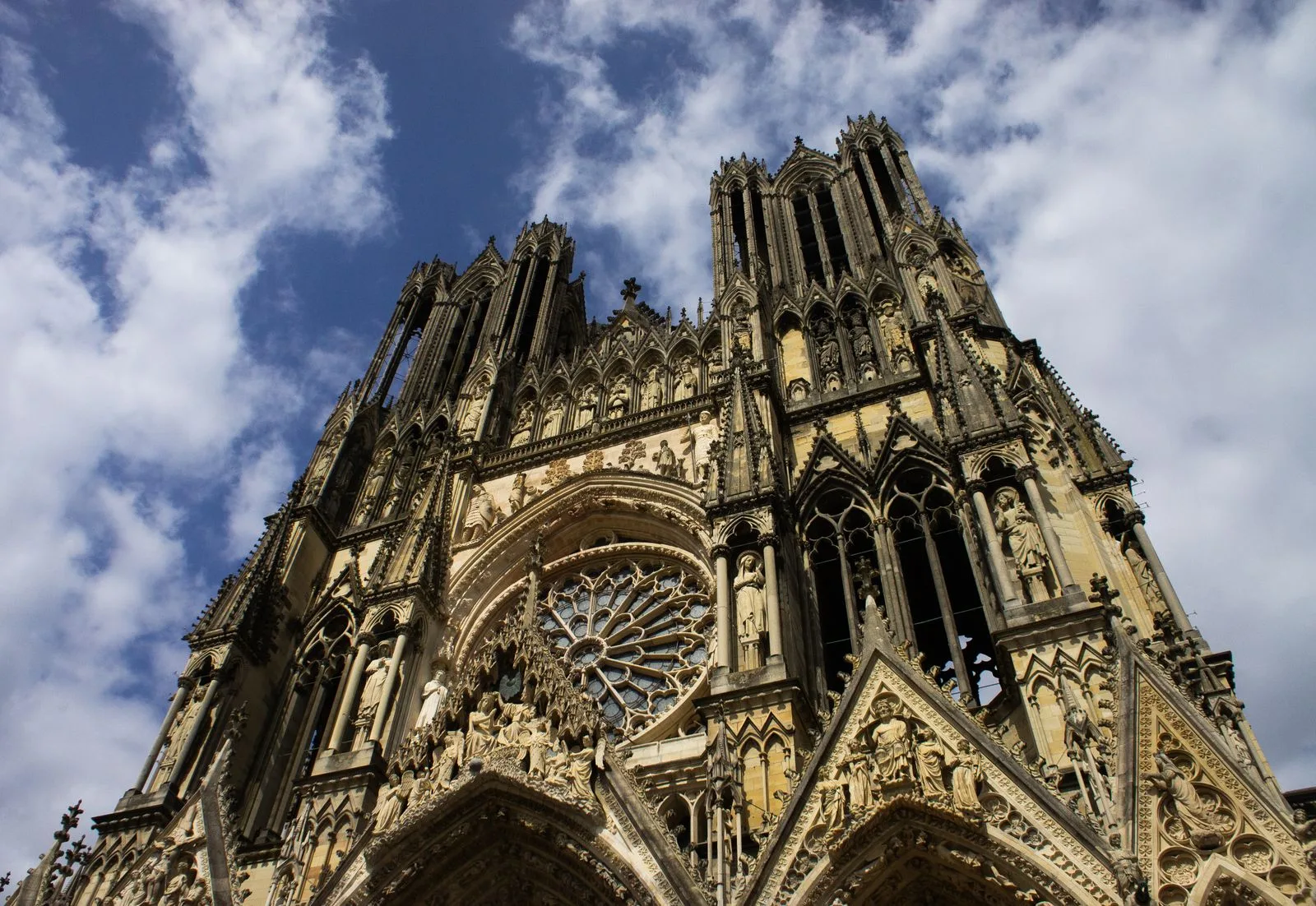 Façade gothique de la cathédrale Notre-Dame de Reims vue en contre-plongée sous un ciel nuageux