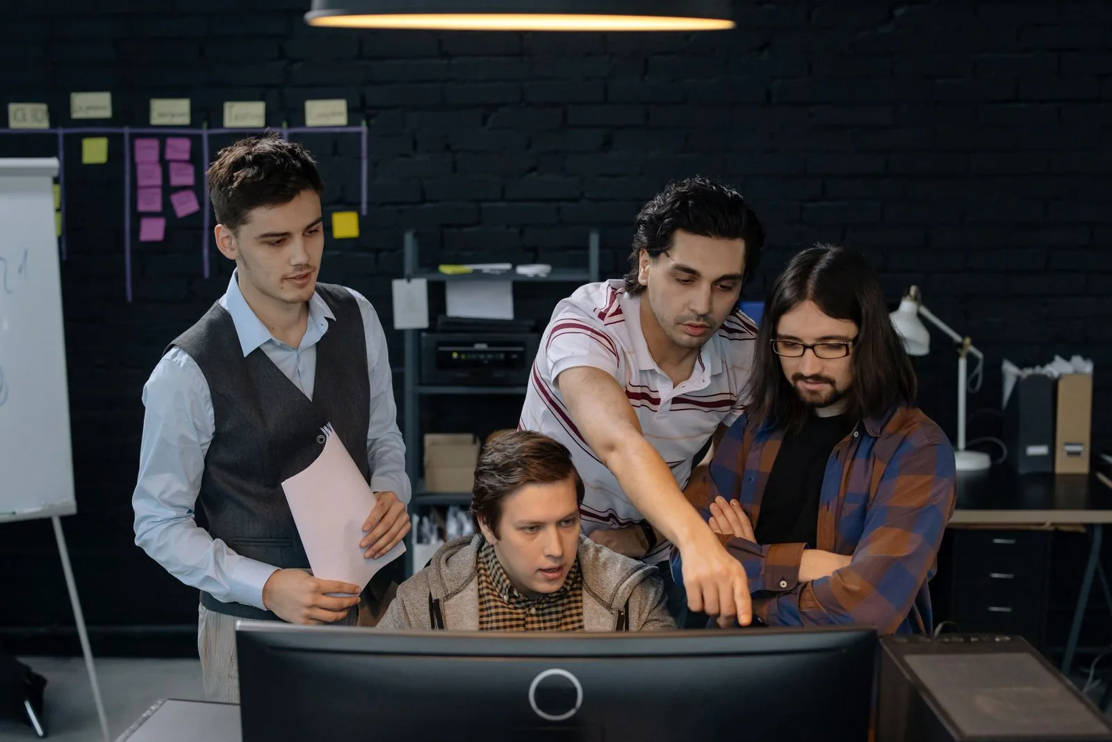 Quatre développeurs examinent ensemble un écran devant un tableau de post-it de sprint