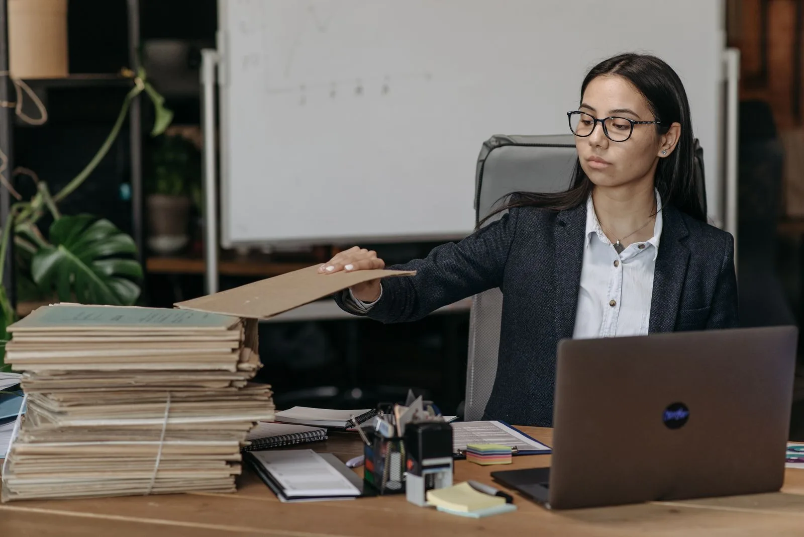 Auditrice qui empile des dossiers cartonnés sur son bureau, ordinateur portable ouvert à côté