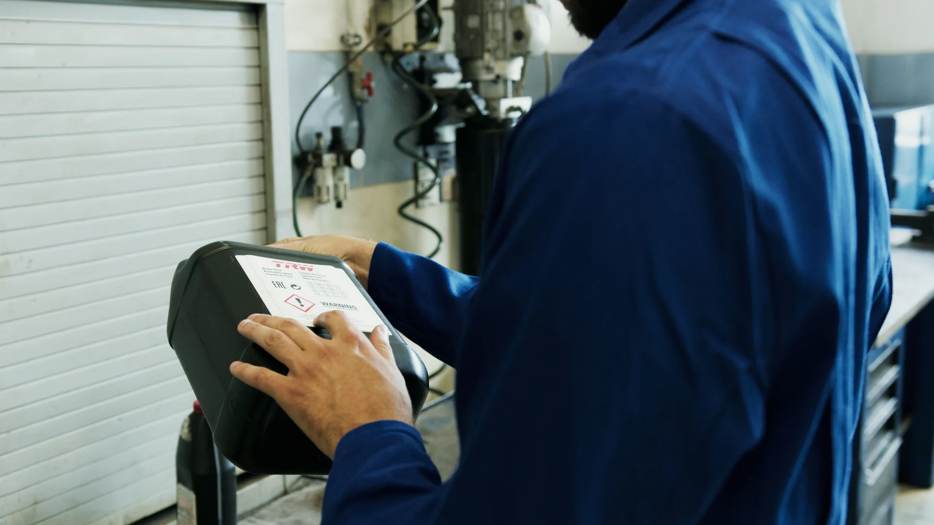 Technicien en bleu de travail tenant un appareil de diagnostic dans un atelier de maintenance