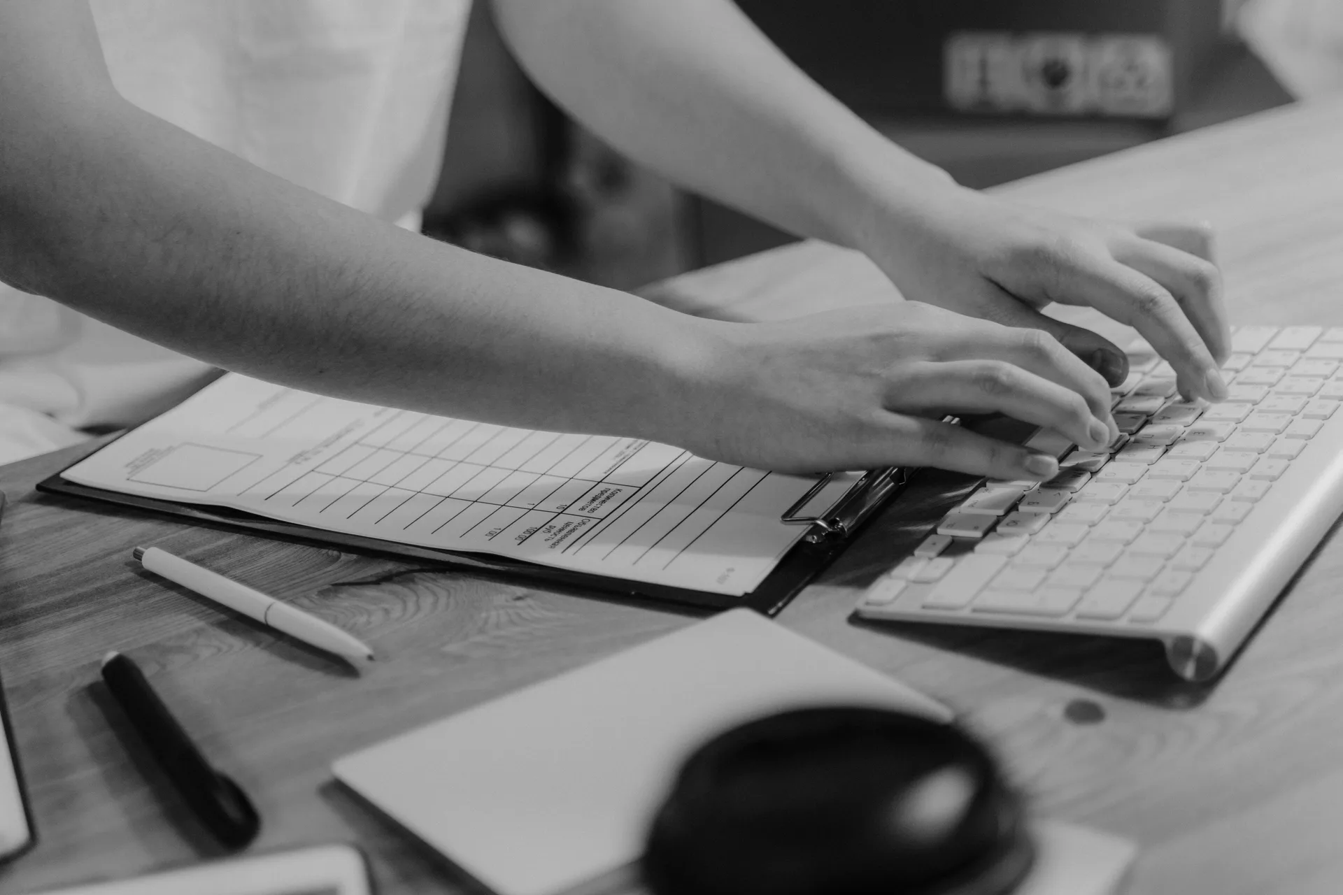 Des mains saisissent au clavier les informations d'un formulaire papier posé sur un porte-bloc